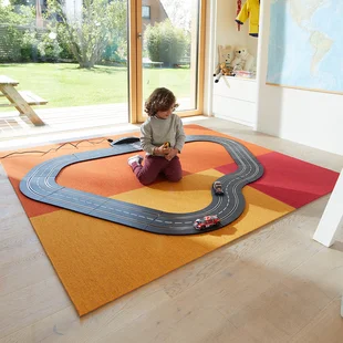 Kinderteppich - Ein Teppich in fröhlichen Farben liegt im Kinderzimmer. Ein Kind spielt darauf mit einer Rennbahn.