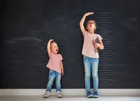 Two children sisters play together. Kid measures the growth on the background of blackboard. Concept of education. - Two children sisters play together. Kid measures the growth on the background of blackboard. Concept of education.